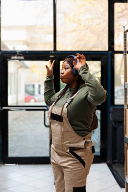 Afrika kökenli Amerikalı bir depo çalışanı, kulaklık takıyor, karton kutularla eşyaları denetliyor. Stok işçisi, envanterde çalışmaya başlamadan önce müzik dinleyip eğleniyor.