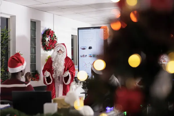 クリスマスの衣装を着たスピーカーは お祝いの飾り付けボードルームで会社の労働者のビジネスインサイトを教えます 冬休みシーズン中に従業員にデータの可視化を示すエキスパート講師 — ストック写真