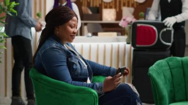 Otelin dinlenme odasında sosyal medya metinlerini okumak için akıllı telefon uygulaması kullanan turist internet sayfasına telefonla bakıyor. Afro-Amerikan kadın tatilde. El kamerasıyla..