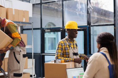 Depo çalışanları grubu bilet kontrolü yapıyor ve nakliye için paket hazırlıyor. Tüm siyah depo çalışanları müşteri siparişlerini depoda seçerken sohbet ediyorlar.