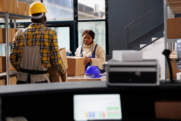 Woman package handler putting cardboard box on table and preparing parcel before shipment in warehouse. Deliver service african american worker packing carton in storage room