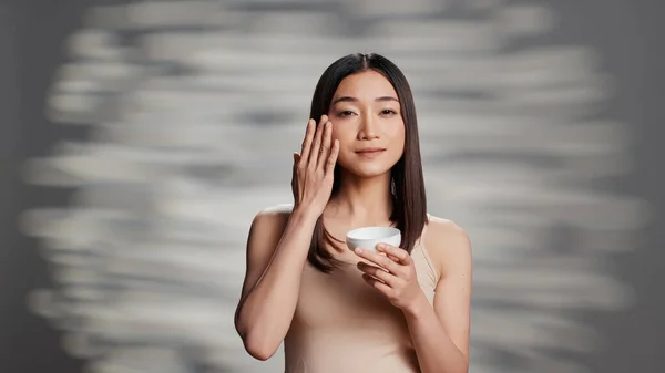 Glowing Asian Lady Applying Moisturizing Face Cream Promote Skincare Routine — Stok fotoğraf