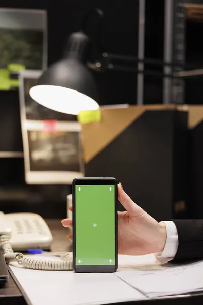 Private detectives showing mobile phone with green screen mock up chroma key isolated display. Criminology employees working late at night at confidential criminal case in evidence room.