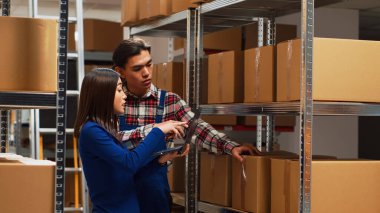 İşçi takımı raflardaki karton kutuları analiz ediyor, depodaki malları kontrol ediyor. Erkek ve kadın dizüstü bilgisayar kullanarak ürün nakliyatı, küçük işletme geliştirme.