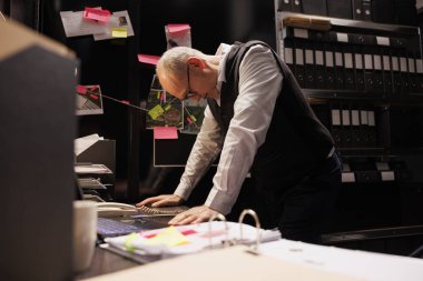 Suç soruşturmalarında fazla mesai yapan müfettiş arhiv odasındaki kanıt dosyalarını analiz ediyor. Kıdemli özel dedektif kriminoloji raporlarını kontrol ediyor, polis merkezinde duruyor.