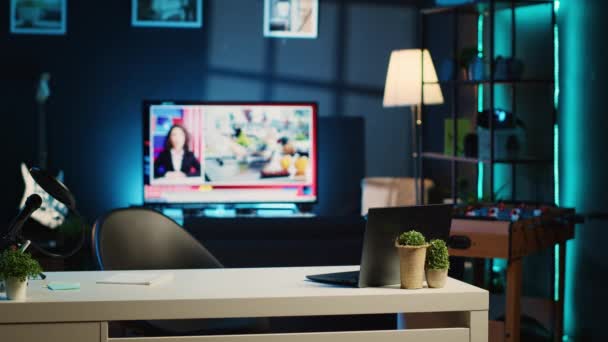 空のホームスタジオのインテリアにラップトップ マイク ミニハウスプラントを備えたワークデスクのパンニングショット コンテンツ制作機材が充実したアパート バックグラウンドでのテレビニュース放送 — ストック動画