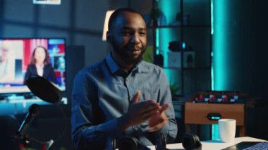 Loş ışıklı oturma odasındaki içerik yaratıcısı çevrimiçi yayın platformları için kablosuz kulaklık incelemesi yapmak için kamera kullanıyor. Medya yıldızı internet şovu sunuyor, müzik dinleme aygıtı açıyor