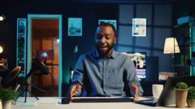 Oturma odasındaki BIPOC içerik yaratıcısı çevrimiçi yayın platformları için klavye incelemesini filme almak için kamera kullanıyor. Çevrimiçi yıldız internet şovu sunuyor, kablosuz bilgisayar kenarlarını açıyor