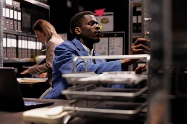 Afrika kökenli Amerikalı muhasebeci şirket dosyalarını düzenliyor, depolama odasındaki yönetim araştırmalarını analiz ediyor. Resmi takım elbiseli bir işadamı şirket deposundaki muhasebe raporunda fazla mesai yapıyor.