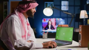 Müslüman adam izole edilmiş bir ekranda sosyal medya paylaşımlarını kontrol ediyor. Daire ofisindeki krom anahtar cihazdan internet sitelerine girip arka plan gürültüsü olarak TV kullanan serbest çalışan kişi