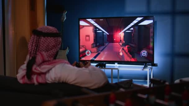 テレビでシングルプレイヤーのビデオゲームをプレイするアラビアの男は 仕事で長い一日の後にリラックスします ゲームコンソールでサイエンスフィクションシューティングゲームを楽しむ中東のゲーマー 楽しい — ストック動画