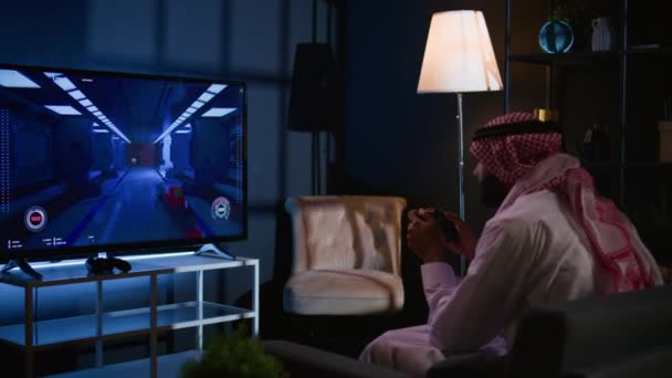 テレビでシングルプレイヤーのビデオゲームをプレイするアラビア人男性 リビングルームでリラックス ゲームコンソールでサイエンスフィクションシューティングゲームを楽しむ中東のゲーマー 楽しい ハンドヘルドカメラショット — ストック動画