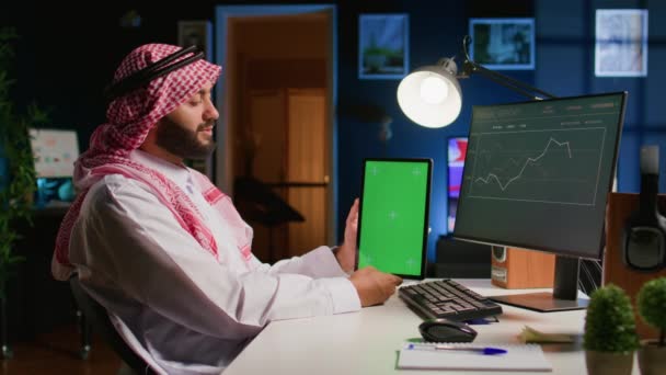 在公寓办公室的穆斯林工人拿着彩色按键平板电脑 将数据与计算机上的商业报表进行交叉扫描 手握模拟数字设备的微笑创业者完成工作任务 — 图库视频影像