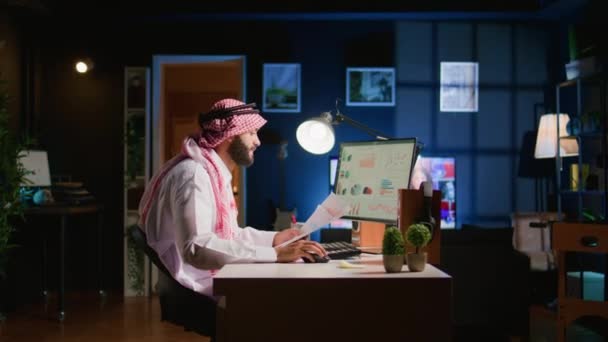 Muzułmański Telepracownik Krzyżujący Dane Statystyczne Papierkową Robotą Podczas Zdalnej Pracy — Wideo stockowe