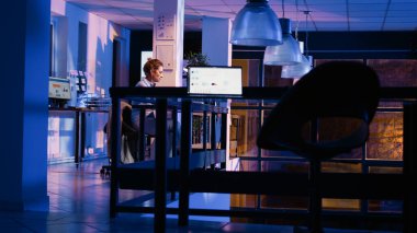 Executive assistant leaving desk job after hours, working late at night after analyzing diagrams report in office. Young business woman planning financial development on pc. Handheld shot.