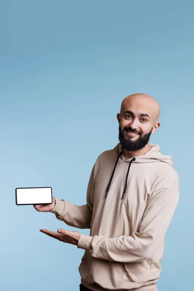 スマートフォンに白い画面を表示する笑顔の陽気なアラブの男性は 肖像画をモックアップするマーケティングのために アプリのプロモーションやカメラを見るための空のディスプレイで携帯電話を保持しているケアフリー広告主 — ストック写真