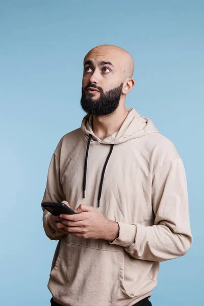 スマートフォンでテキストを送信し 年金表現でソーシャルメディアネットワークを使用する思慮深いアラブ人男性 携帯電話で送信する前にメッセージについて考えている間に疑問を抱く若者 — ストック写真