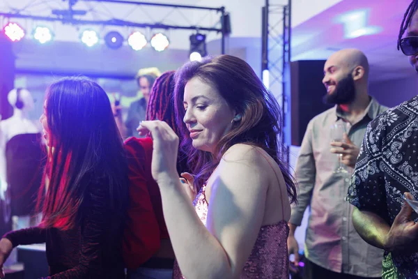 Young woman partying and dancing in crowded nightclub while attending social gathering event. Clubber girl moving to live music rhythm on dancefloor surrounded with people