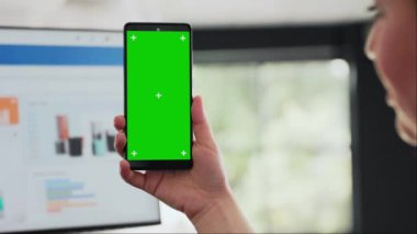 Kadın akıllı telefonu masasında tutuyor, mobil cihazdaki izole edilmiş yeşil ekran şablonunu kontrol ediyor. Modern düzen teknolojisi, kromakey kopyalama uzayı üzerinde çalışan bir işletme yöneticisi. Kapat..