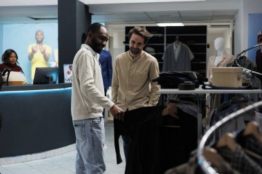 Gülümseyen müşteriler ve asistanlar rafları karıştırırken giyim tarzlarını tartışıyorlar. Afrikalı Amerikalı adam alışveriş merkezinin müşterilerine kıyafet gösteriyor ve moda tavsiyesi veriyor.