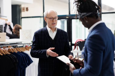 Yaşlı bir adam resmi giysiler için işçi arıyor, Afro-Amerikan çalışan Showrrom 'daki tablet bilgisayardan mal stoklarını kontrol ediyor. Üst düzey müşteri yeni moda koleksiyonuna bakıyor.