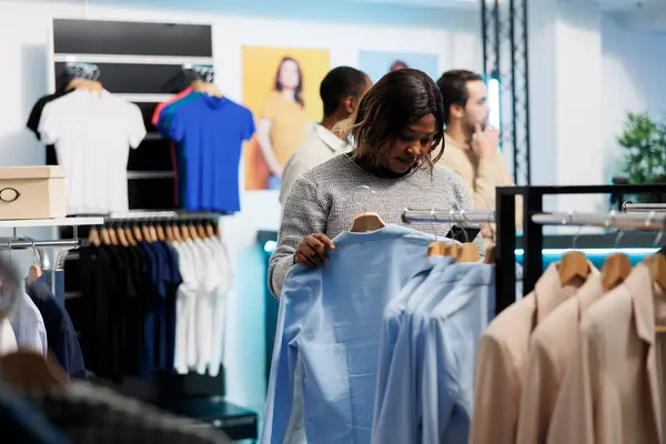 African american woman searching apparel size stock in clothing store online app using smartphone. Shopping mall customer holding mobile phone and checking garment on website