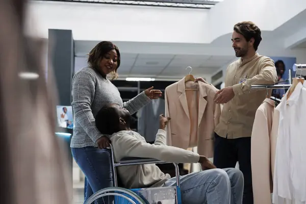 衣料品店で買い物しながらガールフレンドとジャケットを選ぶ身体障害を持つ男 モール アフリカ系アメリカ人の顧客 車椅子で妻と服を選択 — ストック写真