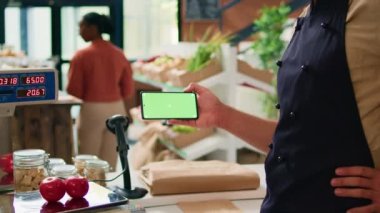 Tezgahta telefon yeşil ekranlı bir tüccar, mobil cihazda izole edilmiş kromakey ekran sunuyor. Çiftçi ve tedarikçi, modern kopyalama teknolojili şablon kullanıyor.