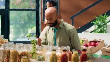 Genç adam çevre dostu mağazaları keşfediyor, yeniden kullanılabilir ambalajlı çeşitli organik ürünlere göz atıyor. Orta Doğulu müşteri kavanozlarda makarna ve tahıl arıyor..