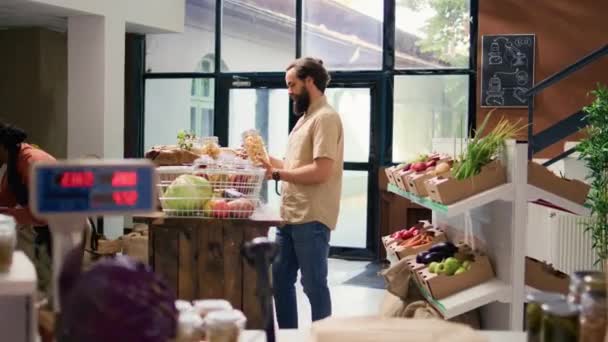 エコスーパーマーケットで買い物をする若いクライアントは 地元の農場で栽培された新鮮な天然果物や野菜を見ています バイオゼロ廃棄物オーガニックショップを訪問する男無料のパスタや穀物を購入する — ストック動画