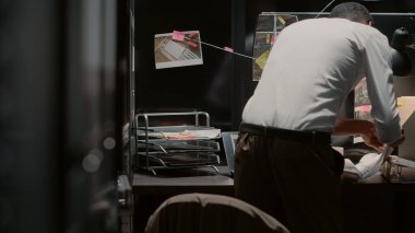 Afrika kökenli Amerikalı bir kanun adamı olay odasında özel soruşturma yürütmeye çalışıyor. Genç bir polis memuru haritadaki fotoğrafları ve adli kanıtları inceliyor..