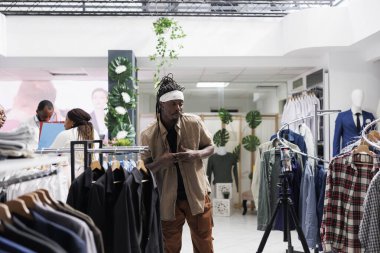 Moda mağazasında tripodun üzerinde akıllı telefon kullanarak giyim markası için promosyon videosu kaydeden Afro-Amerikan bir Amerikalı. Blog yazarı takipçileri için sosyal medyada erkek giyim reklamları yapıyor