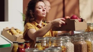 Sürdürülebilir sıfır atık süpermarketindeki vejetaryen kadın alışveriş sepetine koymadan önce elma kokluyor. Mahallenin bakkal dükkanındaki müşteri yerel meyve topluyor.