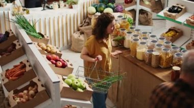 Sıfır atık mağazası müşterisi koridorlarda dolanıp alışveriş sepetine sağlıklı doğal kiler zımbaları, hava aracı çekimleri ekliyor. Yerel bakkal müşterisi koruyucuları ücretsiz toplu gıda ürünleri alıyor