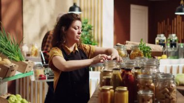 Gülümseyen sıfır atık süpermarket sahibinin portresi, iklim etkisini azaltmak için kirletici olmayan cam kaplar kullanıyor. Yerel bakkal dükkanında ürünleri düzenleyen neşeli bir tüccar