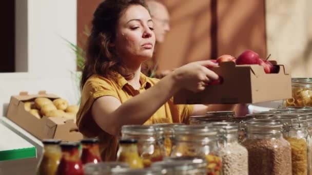 持続可能なゼロ廃棄物スーパーマーケットのビーガン女性は ショッピングバスケットにそれらを追加する前にリンゴを嗅ぐ 地元の食料品店のクライアントが地元で栽培された果物を選ぶ — ストック動画