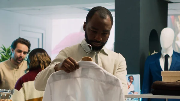 アフリカ系アメリカ人の男性が衣料品店の棚にシャツをチェックし ショッピングモールから商品を購入しようとしています 小売市場のブティックを訪問ファッショナブルなライフスタイルを持つ男性クライアント — ストック写真