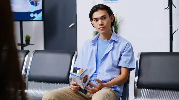 Portrait of nervous patient waiting to attend checkup visit with doctor, sitting in hospital lobby. Asian man with disease preparing for examination during checkup visit consultation. Medicine concept