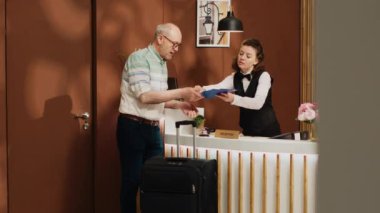 Resepsiyondaki kıdemli adam beş yıldızlı otel lobisinde rutin kontroller yapıyor. Resepsiyonda kayıt formlarını imzalayan gezgin, tatil gezisinde oda servisini ve konforları kontrol ediyor..