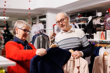 İki müşteri elbise mağazasında ceketleri inceliyor, askılardaki ceketleri inceliyor ve hediye almak için alışveriş merkezini ziyaret ediyor. Erkek ve kadın indirimli bir kıyafet seçmeye çalışıyor, xmas sezonu..