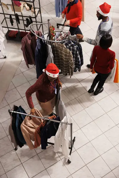 Retail clerk organizing merchandise on holders in shopping center store, helping clients with finding right christmas gifts at mall. Woman store employee moving hangers of items around.