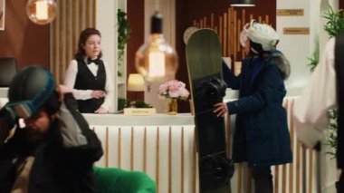 Kadın çalışanlara kayak hizmetlerini soruyor, dağ otelindeki karlı yamaçlardan kaymak için sabırsızlanıyor. Asyalı gezgin, resepsiyonistle snowboard ve kış sporları hakkında konuşuyor..