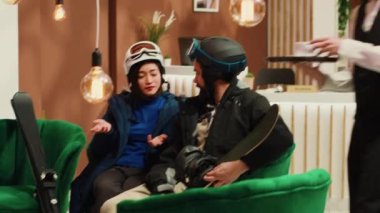 İnsanlar, başarılı kayak ve snowboard aktivitelerinden sonra kış sporu kıyafetleriyle ilgili düşüncelerini paylaşıyorlar. Bir adam ve bir kadın dağ kayak merkezinde seyahat ediyorlar. El kamerasıyla..