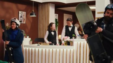 Turistler kış tatili için kayak merkezinin lobisine gelip resepsiyonda oda kontrolü için bekliyorlar. Dağ otelinde kayak ya da snowboard ekipmanları taşıyan çeşitli müşteriler..