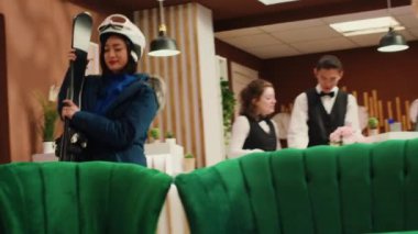 Gezginler, kış tatili için kayak tesisi lobisine gelip oda kontrollerini bekliyorlar. Alpine Otel 'de kar giysileri içinde kayak ya da snowboard ekipmanları taşıyan çeşitli insanlar. El kamerasıyla..