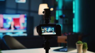Çevrimiçi platformlar için video çekmek için loş ışıklandırılmış stüdyo dairesindeki medya yıldızları tarafından kullanılan tripodun üzerindeki kameranın aşırı yakın çekimi. İçerik oluşturucu tarafından çekimleri yakalamak için kullanılan boş odada kayıt cihazı
