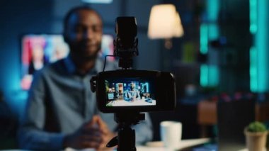 Çevrimiçi yayın platformları için video çekimleri için kullanılan rahat ev stüdyosundaki profesyonel kayıt cihazına yakın çekim. Bulanık arkaplandaki etkili hayran kitlesini selamlıyor, kameraya odaklan