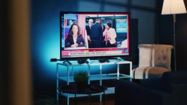 TV 'nin yakın plan çekimleri gece açık bırakılmış rahat ve loş bir dairede haber kanalını gösteriyor. Ev yapımı eğlence sistemi, oturma odasında mavi ışıkla aydınlatılmış televizyon haberlerini gösteriyor.