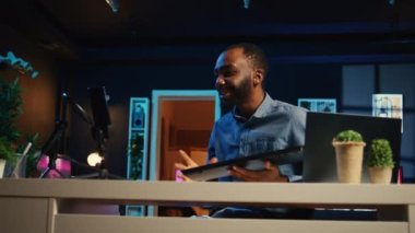 Çevrimiçi yayın platformları için loş ışıklandırmalı stüdyo filmleri klavye ve fare setinin içerik tasarımcısı. Afrikalı Amerikalı adam internet şovu sunuyor, kablosuz bilgisayar bağlantılarını açıyor.