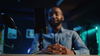 Çevrimiçi platformlar için video çekmek için loş ışıklı ev stüdyosunda çevrimiçi yıldız tarafından kullanılan cep telefonunu ve mikrofonu kapat. Telefon, Afrikalı Amerikalı etkileyiciler tarafından çekimleri kaydetmek için kullanılıyor.